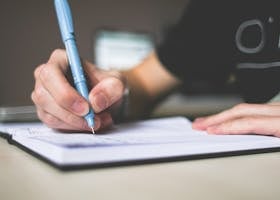 Person Holding Blue Ballpoint Pen Writing in Notebook